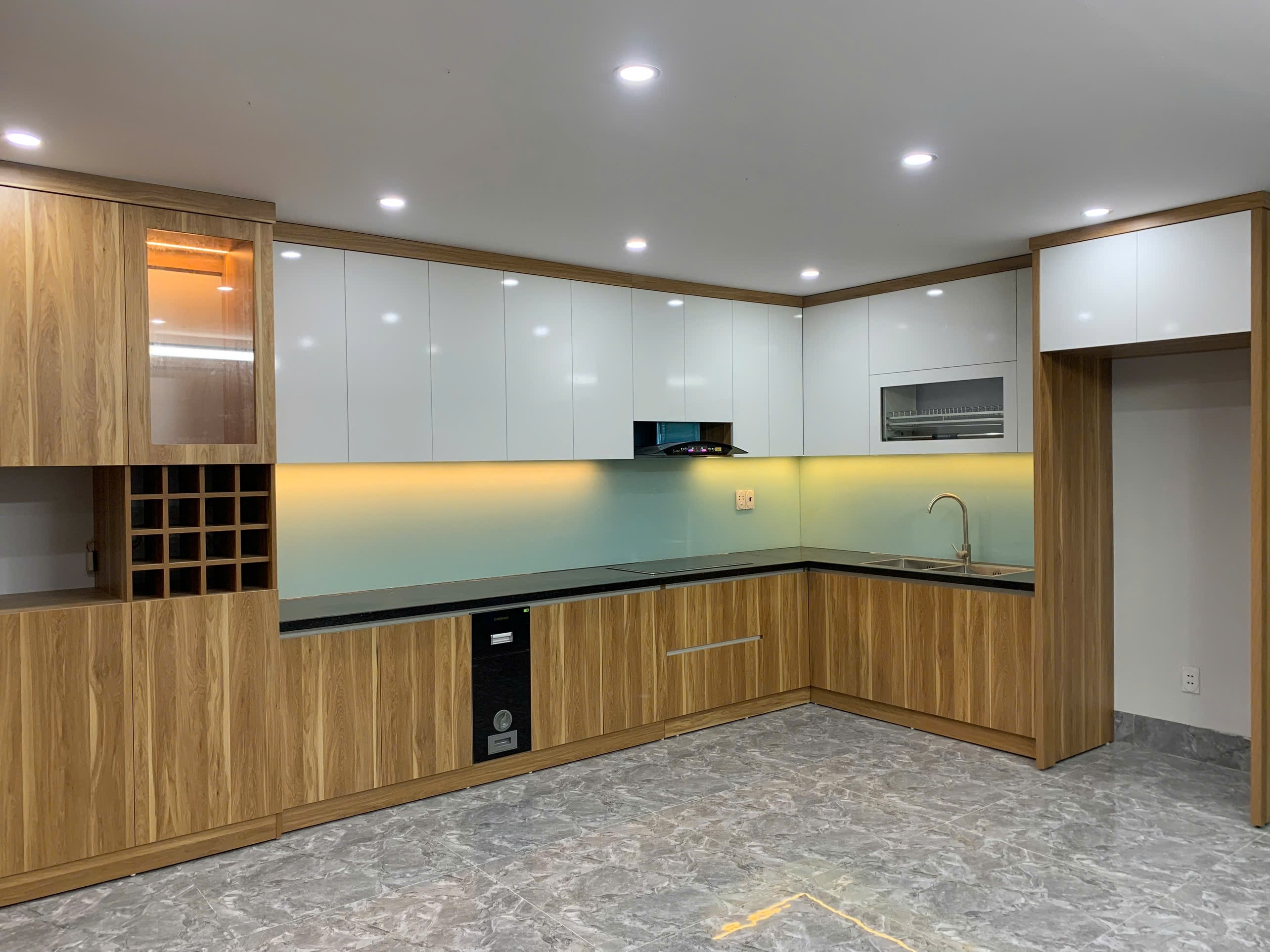 Bếp chữ L lớn tủ dưới vân gỗ, tủ trên acrylic trắng, kính vàng ấm - Bếp chữ L lớn tại Khu vực Nam Định